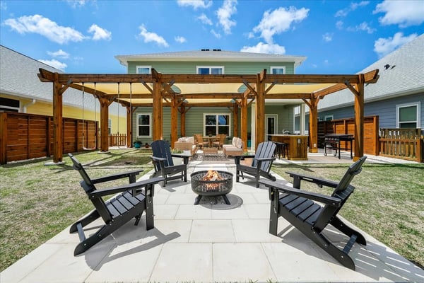 Backyard patio with fire pit, black Adirondack chairs, wooden pergola, and green house with garage