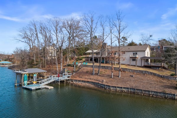 Waterfront property with white house, boat dock, and bare trees along calm lake